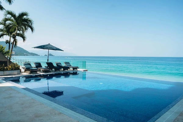 Infinity pool with lounge chairs and umbrella overlooking turquoise ocean and palm trees