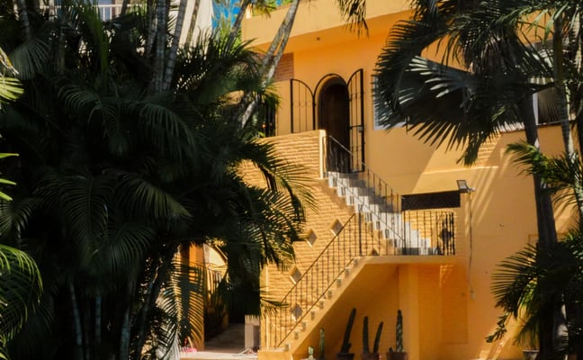 Yellow colonial-style house with swimming pool and palm trees in courtyard
